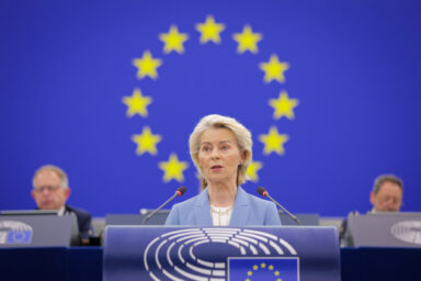 Ursula von der Leyen speaking at the podium of the European Parliament in Strasbourg, with the EU flag behind her