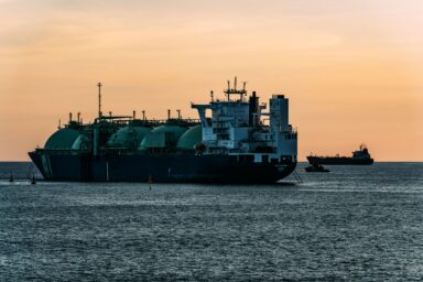 LNG carrier with spherical tanks anchored at sea at sunset, with another tanker on the horizon