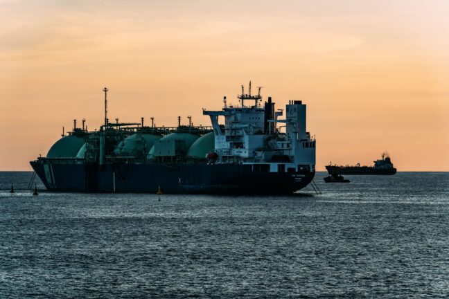 LNG carrier with spherical tanks anchored at sea at sunset, with another tanker on the horizon