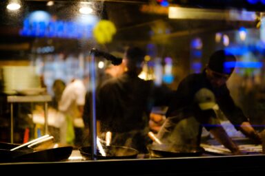 Cooks working at a stove in a restaurant kitchen at night, seen through a steamed-up window