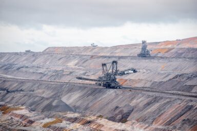 Bucket-wheel excavator working in a vast open-pit mine with layered terraces under a cloudy sky