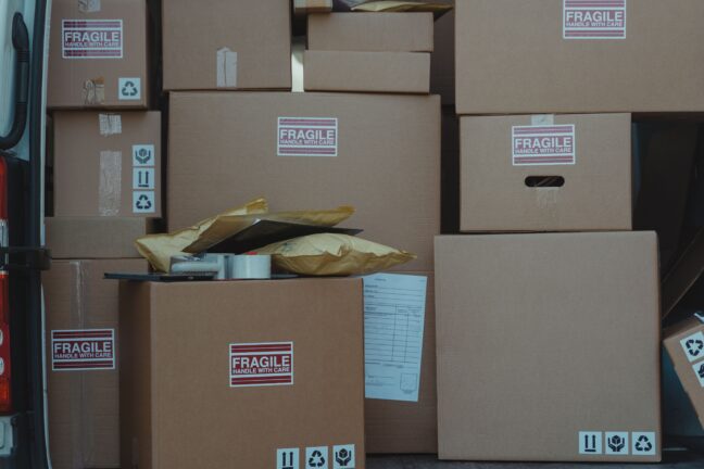 Stacked cardboard boxes with fragile and recycling labels next to a delivery van