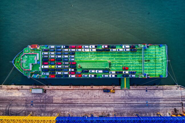 Aerial view of a car carrier ship loaded with rows of cars, moored at a port quay