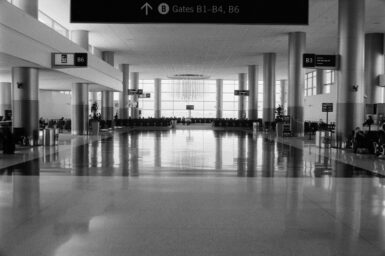 Black-and-white view of an airport departure hall with a sign pointing to the gates