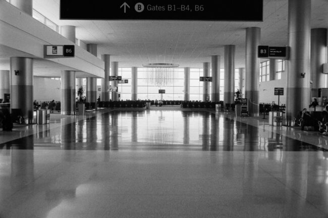 Black-and-white view of an airport departure hall with a sign pointing to the gates